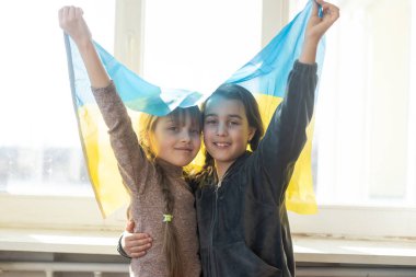 Little girls with Ukrainian flag in front of a window. The little girls waves the national flag while praying for peace clipart
