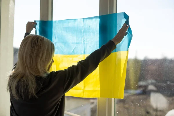 Uma mulher pendura uma bandeira de ucraniano na janela — Fotografia de Stock