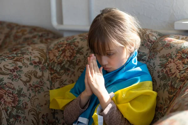 Klein meisje vluchteling bidt met Oekraïense vlag. — Stockfoto