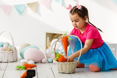 Paskalya 'ya hazırlanıyorum. Paskalya yumurtası tutan ve arka planda süslemelerle gülümseyen sevimli küçük kız.