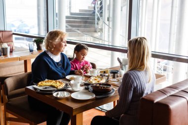 Çocukluk ve insan konsepti - açık kaşık yiyen mutlu büyükanne ve küçük kız açık kafe veya restoran
