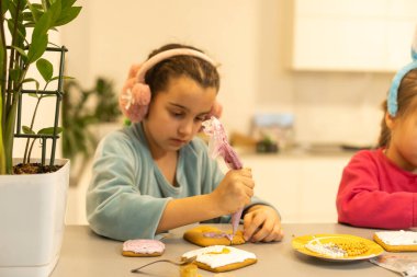 İki güzel kız kardeş, ahşap bir masada lezzetli pastalar süsleyip yiyorlar.