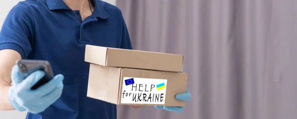 A man holds a box of aid for Ukrainian refugees and poor citizens who find themselves in a war between Ukraine and Russia. Humanitarian aid concept. Donate for refugees. — Stock Photo, Image