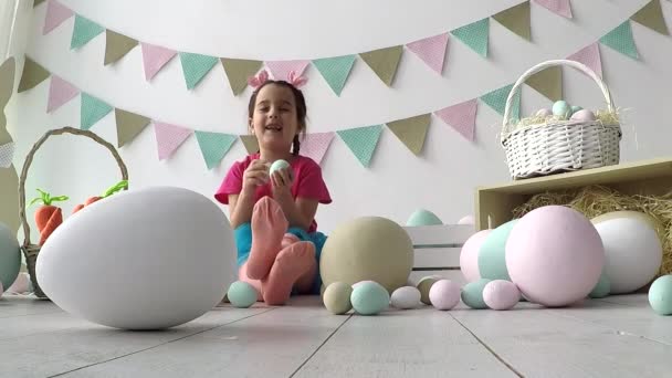 Великодня дівчинка грає з великодніми яйцями, на підлозі багато великоднього декору — стокове відео