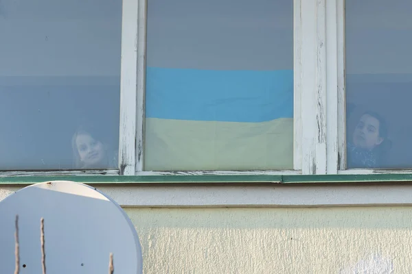 Egy kislány a ház ablakában egy festett sárga-kék zászló Ukrajna, béke Ukrajnában, megállítani a háborút, tiltakozás és hazafi, otthon Ukrajna. — Stock Fotó