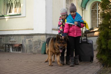 Ukrayna bayrağı taşıyan iki küçük kız, bavul, köpekler. Ukrayna savaş göçü. Eşyaları bir bavulda toplamak. Ukrayna bayrağı, yardım et. Krizin, askeri çatışma..