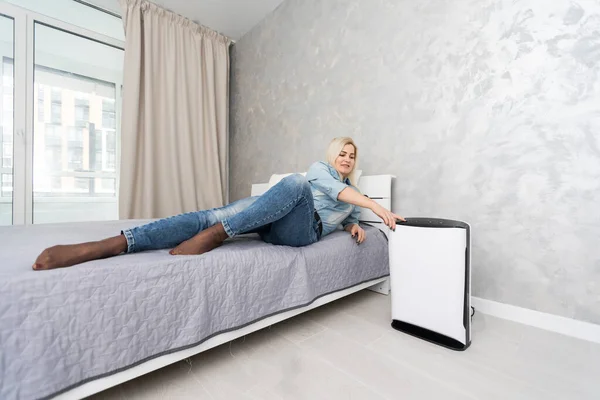 woman turning on and using the modern air purifier in the living room, air purifier is a popular appliance - household electricity. Air purifier can help to purify the air.