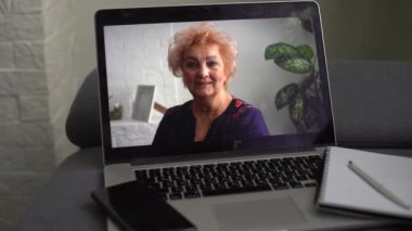 Mutlu olgun 60 'lı yılların kadın portresi. Gözlüklü neşeli yaşlı bayan, sıradan, dişlek gülümsemeli kameraya bakıyor, evde poz veriyor, gülüyor. Video çağrısı ekranı