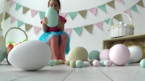 Niña comiendo huevos de Pascua de chocolate sentada en la canasta de vacaciones y un conejo amarillo — Vídeos de Stock