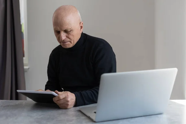 Confuso dai capelli grigi calvo 60 anni maschio in abiti formali navigazione tablet moderno con smarrimento seduto in poltrona a tavola — Foto Stock