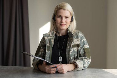 Asker üniformalı seksi sarışın kadın gri duvara poz veriyor.