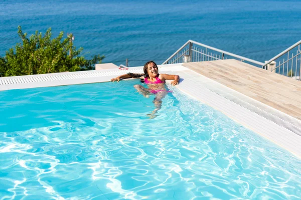 A kislány a játék jumping vízbe nyaralás szigeten tropical beach szabadtéri medencével várja vendégeit. Gyermek a tanulás luxus üdülőhely szabadtéri medence. — Stock Fotó