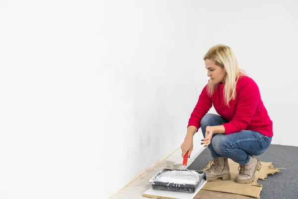 La mujer pintando las paredes con el equipo de rodillos mientras se mueve en el apartamento. Renovación de la casa nueva y concepto de mejora —  Fotos de Stock
