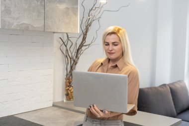 Güzel sarışın bayan dizüstü bilgisayarda çalışıyor. Evdeki koltuğa otur ve pazartesi günü için benzin dükkanlarını kontrol et. Alternatif ofis için teknoloji kadını konsepti.