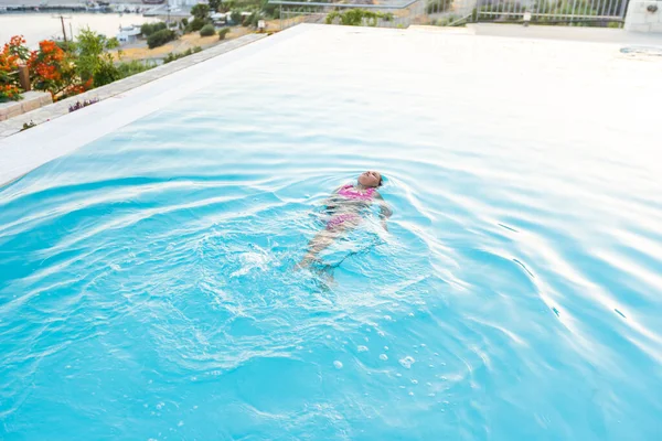 Bambina che gioca in piscina all'aperto saltando in acqua durante le vacanze estive sull'isola di spiaggia tropicale. Bambini che imparano a nuotare nella piscina all'aperto del resort di lusso . — Foto Stock