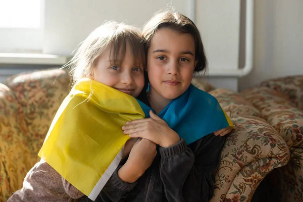 Pencerenin önünde Ukrayna bayrağı taşıyan küçük kızlar. Küçük kızlar barış için dua ederken ulusal bayrağı sallıyorlar. — Stok fotoğraf