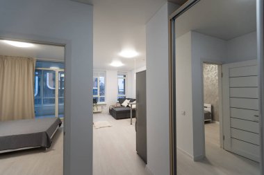Bir sürü beyaz kapısı ve siyah kapı kolu olan küçük ve beyaz apartman koridoru, ahşap zemin ve yatak odası kapıları açık.