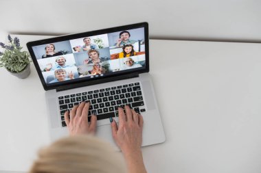 Beyaz kadın öğretmen okul çocuklarıyla video görüşmesinde bilgisayar ve dizüstü bilgisayar kullanıyor. Çevrimiçi eğitim karantina süresince evde tek başına kalıyor..