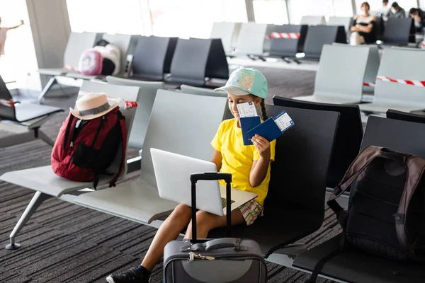 Очаровательная маленькая девочка в аэропорту со своим багажом и ноутбуком — стоковое фото