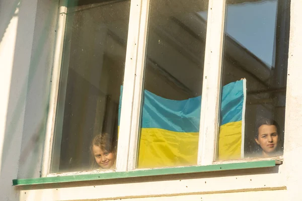 Маленька дівчинка у вікні свого будинку з намальованим жовто-синім прапором України, мир в Україні, зупинка війни, протести і патріотизм, домівка України.. — стокове фото