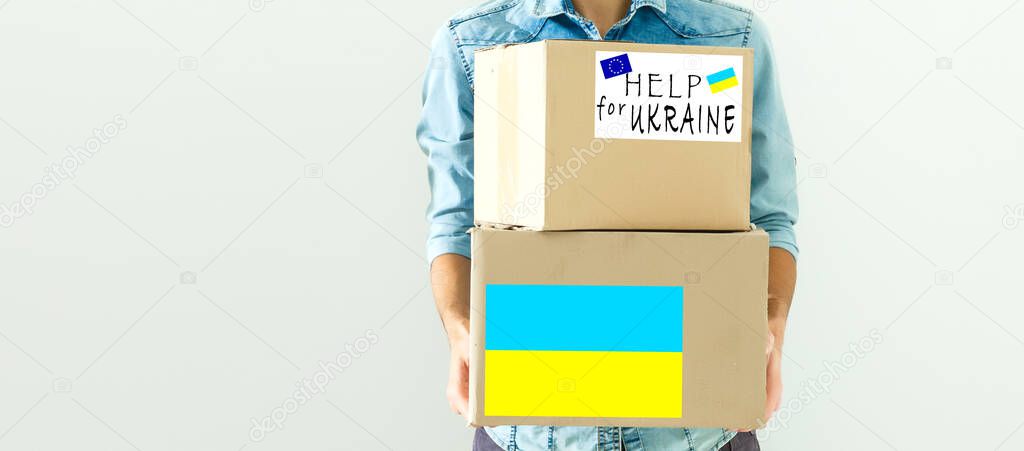 A man holds a box of aid for Ukrainian refugees and poor citizens who find themselves in a war between Ukraine and Russia. Humanitarian aid concept. Donate for refugees.