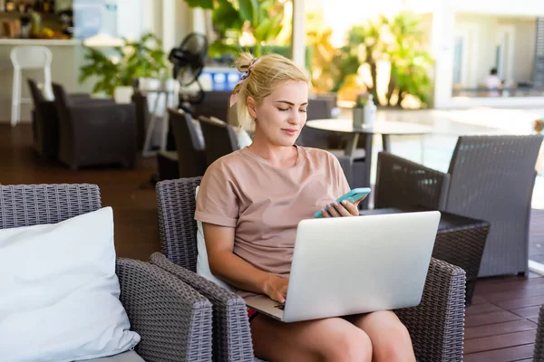 Une photo vue de côté de la femme utilisant un ordinateur portable pour le e-shopping tout en étant assis dans un hall d'hôtel moderne. Une femme blonde portant une robe regarde l'écran — Photo