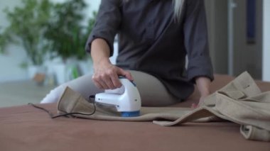 Kadın siyah pantolonun üzerindeki kumaş ve giysilerden topak ve makaraları çıkarmak için makine kullanıyor. Eski şeyleri güncellemek için modern bir elektronik cihaz