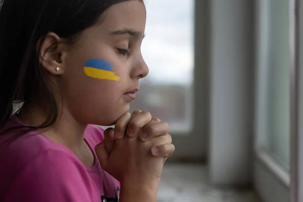 Kleines Mädchen mit ukrainischem Fahnenband beim Gebet. Symbol des Friedens und Gebet für die Ukraine. — Stockfoto