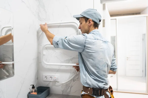 Arbeitender Klempner montiert eine neue verchromte beheizte Handtuchspule an der Wand der Fliesen — Stockfoto