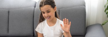 Mesafe öğrenme. Kulaklıklı neşeli küçük kız bilgisayarını kullanarak internetten e-öğrenim sistemini inceliyor..