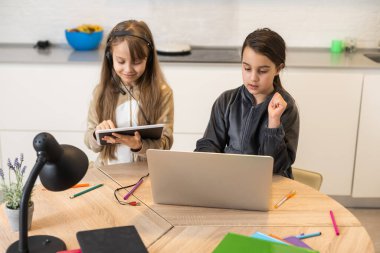 Online eğitim. Kulaklıklı iki liseli kız kardeş dizüstü bilgisayarlardan ders dinliyorlar. Okulda salgın ve karantina var..