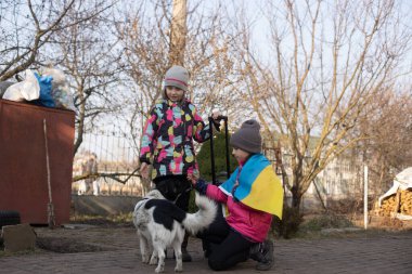 Ukrayna bayrağı taşıyan iki küçük kız, bavul, köpekler. Ukrayna savaş göçü. Eşyaları bir bavulda toplamak. Ukrayna bayrağı, yardım et. Krizin, askeri çatışma..