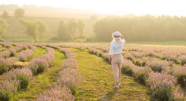 美しい若い健康な女性白いドレスは、夕日の光の下でわら帽子を保持ラベンダー畑を楽しく実行しています — ストック写真