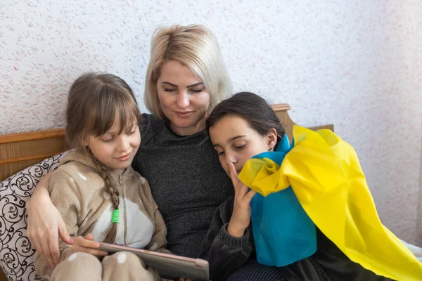 mother and two daughters are reading with the flag of ukraine in bed