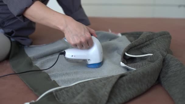 Kvinna använder en maskin för att ta bort pellet och spolar från kläder och tyg på svarta byxor. En modern elektronisk anordning för att uppdatera gamla saker. — Stockvideo