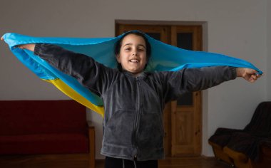 Bombalarla yıkılmış bir duvarın önünde Ukrayna bayrağı taşıyan küçük kızlar. Küçük kızlar barış için dua ederken ulusal bayrağı sallıyorlar.