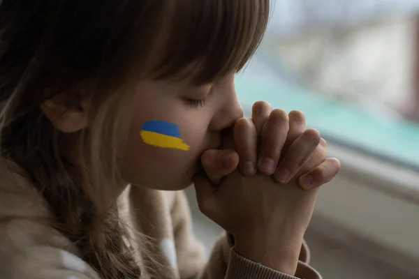 O rosto de uma menina assustada, uma criança chorando, lágrimas fluindo, pintado na bochecha nas cores amarelo-azul da bandeira ucraniana, um pedido de ajuda. Crianças pedem paz. — Fotografia de Stock