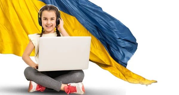 Дівчинка дивиться домашній ноутбук. на фоні українського прапора — стокове фото