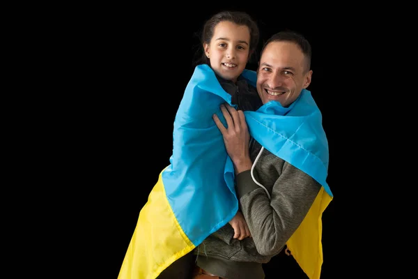 Маленька дівчинка, що тримає український прапор, обнімає свого батька на темному тлі. Стань з Україною. — стокове фото