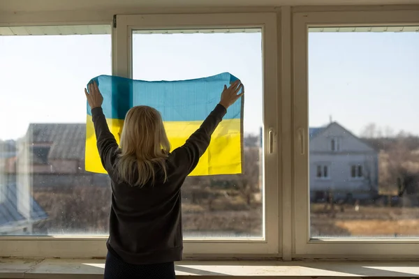 Frau in Ukraine-Fahne gehüllt und aus dem Fenster schauend. Kopierraum — Stockfoto