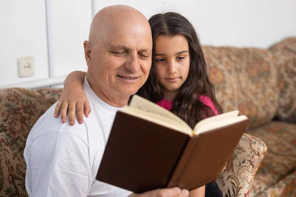 Happy grandfather and granddaughter reading book together at home. Close up. — Stock Photo, Image
