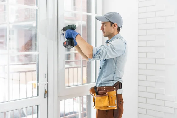 Ezermester beállítja a fehér PVC műanyag ablakot. Egy munkás csavarhúzóval javítja meg az upvc ablakot. házi feladat karbantartása. — Stock Fotó