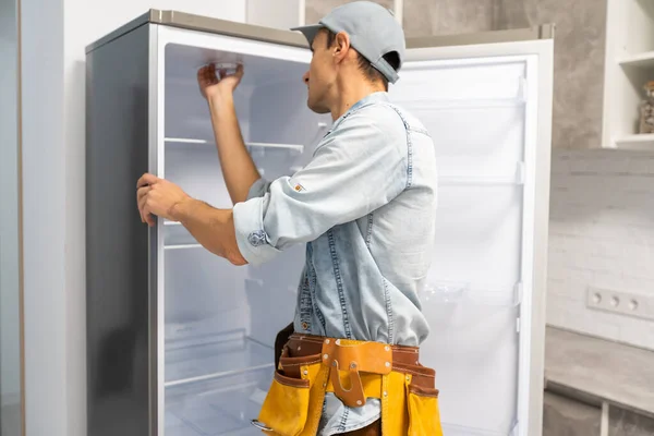 Mladý opravář s pásem nástroj při pohledu na rozbitou ledničku — Stock fotografie