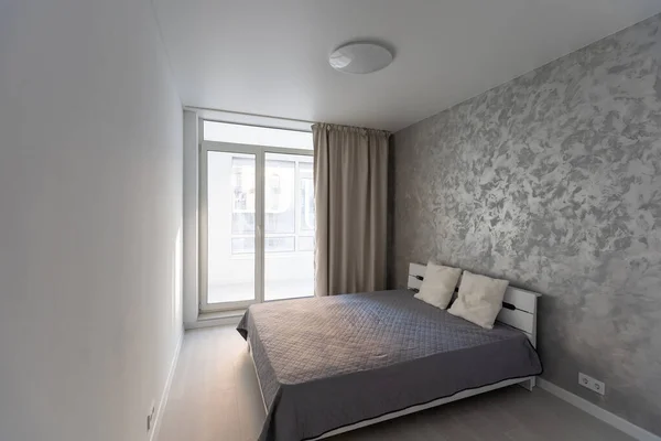 Intérieur élégant de la chambre contemporaine avec un mobilier confortable. Lit pour deux avec couverture et oreillers, miroir et plante en pot sur fond de mur gris dans la maison moderne avec rideaux, éruption de soleil — Photo