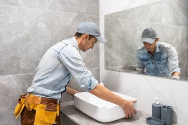 Profesyonel tesisatçı, üniformalı erkek işçi yeni daireye lavabo ve su borusu kuruyor.