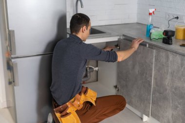 Gülümseyen tamirci, mutfak marangozu tulumlu, mutfak mobilyalarını yerleştirirken kameraya gülümseyen.