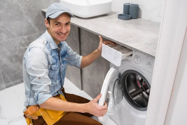 Profesyonel alet çantalı genç ve yakışıklı tamirci banyodaki çamaşır makinesini tamir ediyor.. — Stok fotoğraf