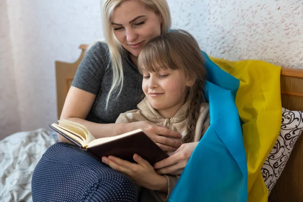 Anya és lánya olvas egy könyvet a zászló ukrán az ágyban — Stock Fotó