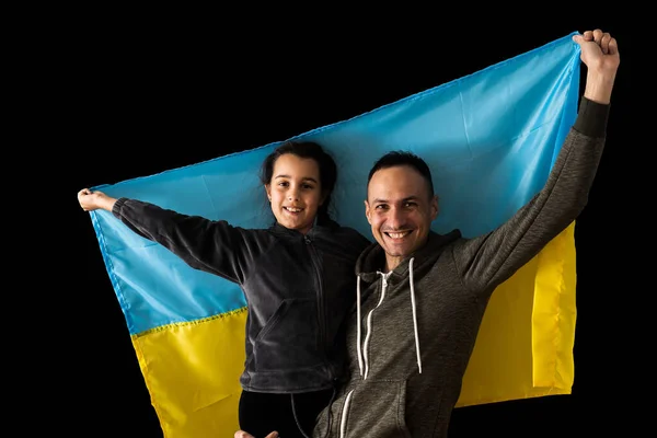 Menina segurando bandeira ucraniana abraçando seu pai no fundo escuro. Fique com a Ucrânia. — Fotografia de Stock