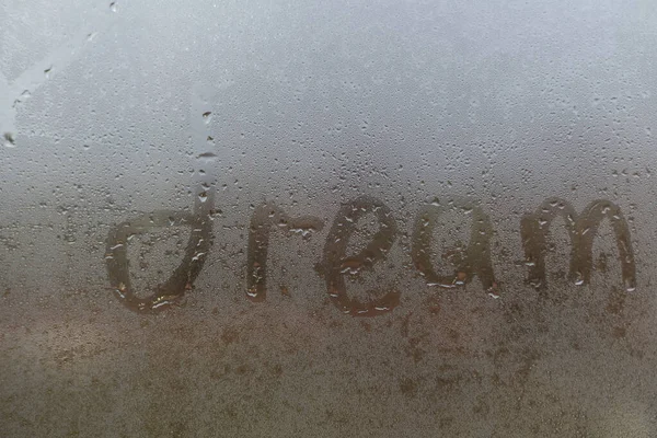 Parola - sogno... Sfondo astratto con gocce d'acqua. Iscrizione su finestra nebbiosa. Testo manoscritto su vetro bagnato. — Foto Stock